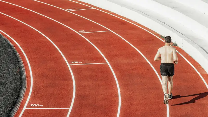 Coureur vu de dos dans le virage d'une piste d'athlétisme rouge