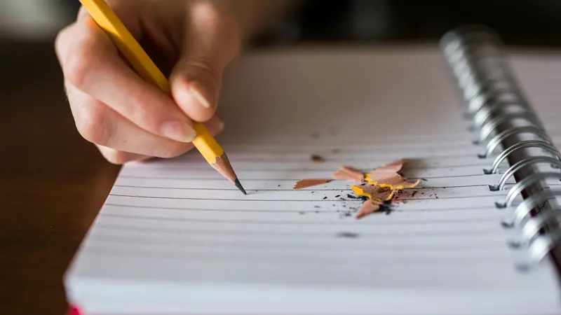 Main qui écrit au crayon dans un carnet à spirale